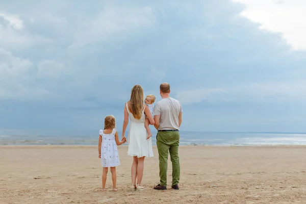 家族: ママ、パパ、曇りの天気で夏の海と雲までの距離を見て二人の女の子 — ストック写真
