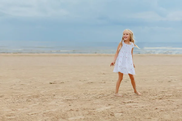 Charming little girl with pigtails jumping on the beach and smil — Stock Photo, Image