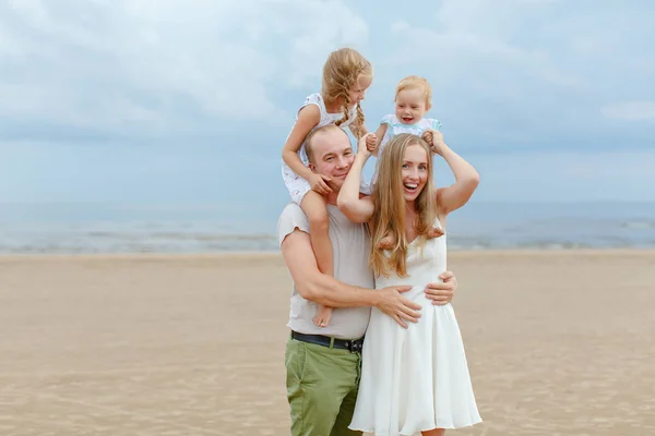 Mãe, pai e duas filhas adoráveis vão ao longo da praia no s — Fotografia de Stock