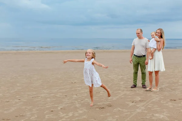 Мама, папа и две прекрасные дочери идут вдоль берега моря в... — стоковое фото