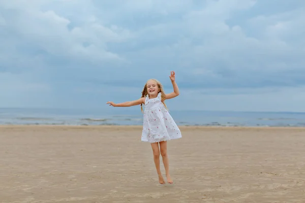 Charmante petite fille avec des nattes sautant sur la plage et smil — Photo