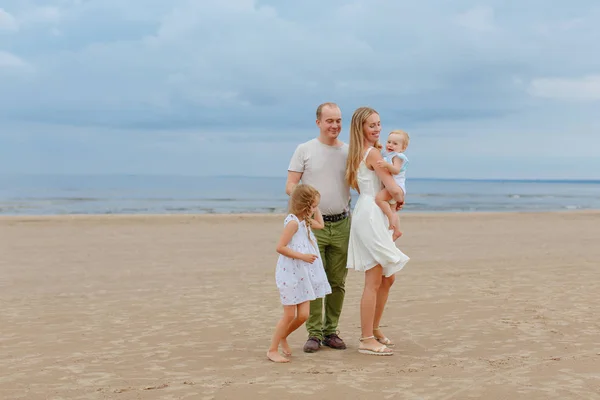 Mãe, pai e duas filhas adoráveis vão ao longo da praia no s — Fotografia de Stock