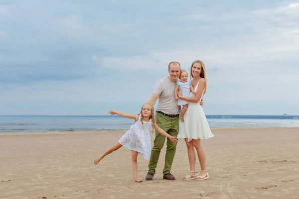 Mãe, pai e duas filhas adoráveis vão ao longo da praia no s — Fotografia de Stock