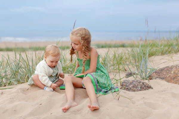Sisters girls sitting next to the sand and playing on the beach — Stock Photo, Image