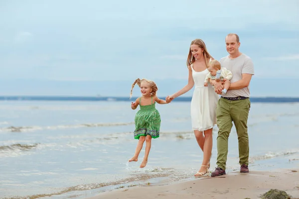 Mamãe, papai e duas filhas salpicam e riem na praia em t — Fotografia de Stock