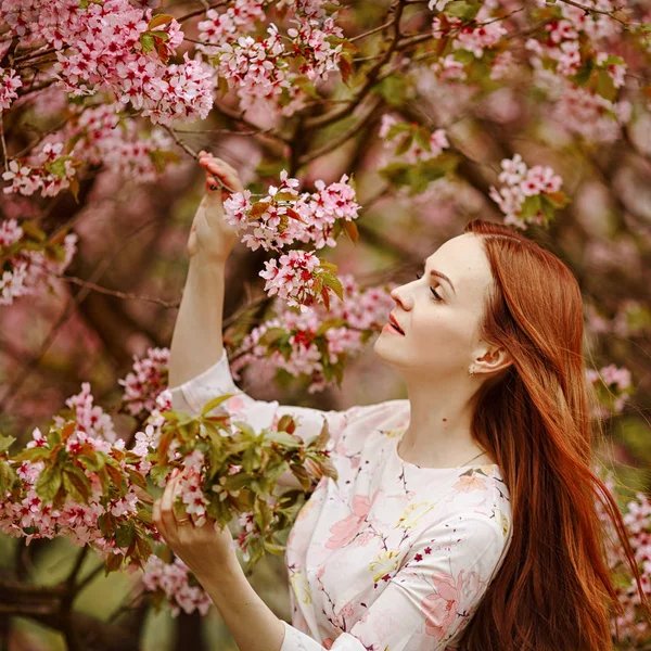 Rothaarige Mädchen auf einem Hintergrund aus rosa Kirschblüten in Sprin — Stockfoto