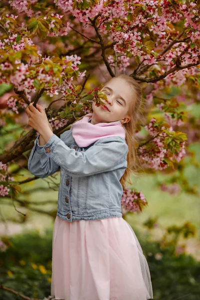 Una linda chica rubia sonríe sobre un fondo de rosa sakura bu — Foto de Stock