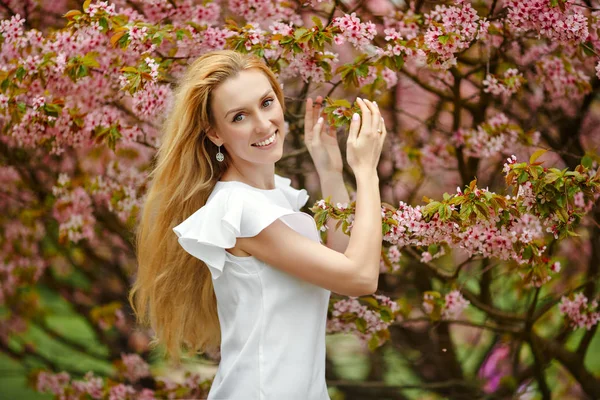 Blond flicka med långa hår ler mot bakgrund av rosa — Stockfoto