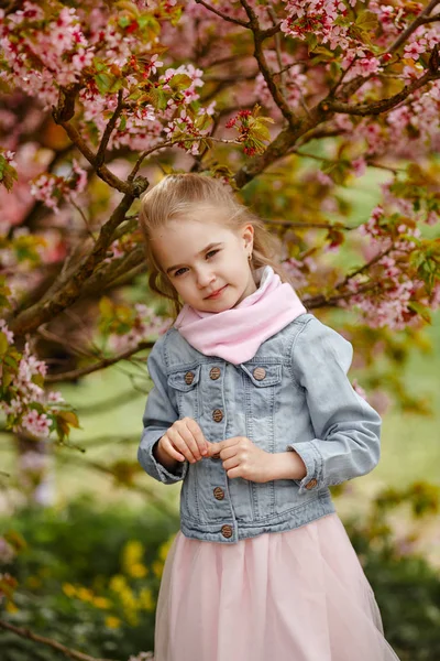 Una linda chica rubia sonríe sobre un fondo de rosa sakura bu — Foto de Stock