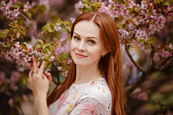 Chica pelirroja sobre un fondo de flores de cerezo rosa en sprin —  Fotos de Stock