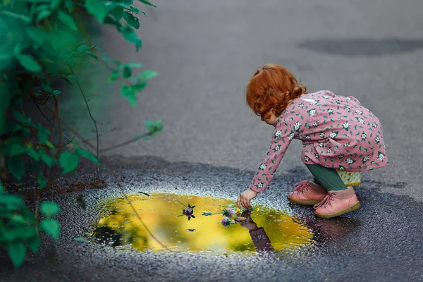 Little beautiful red-haired little girl baby touch the puddle af — Stock Photo, Image