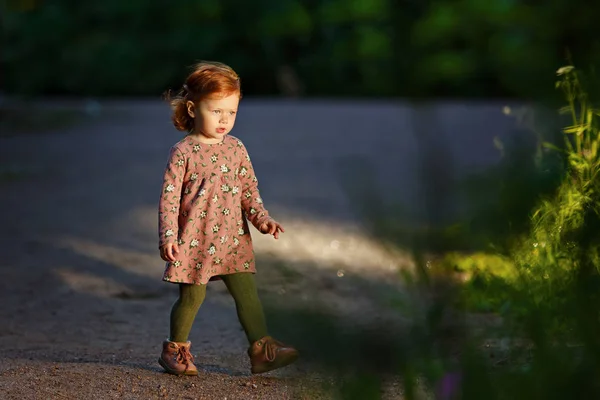 Lille vakre rødhårede lille pike går mot lyset. – stockfoto