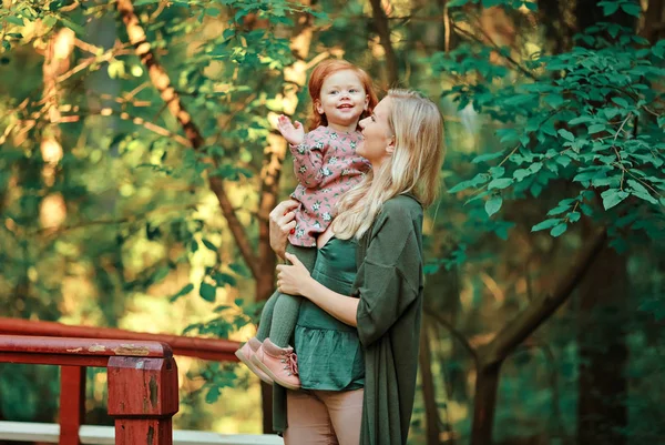Mamá y la hija pelirroja están sentadas y sonriendo al atardecer en — Foto de Stock