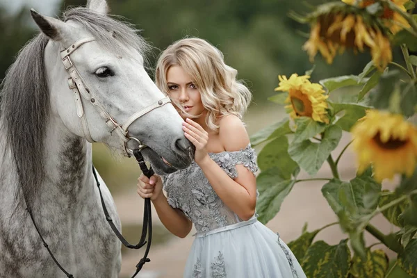 Menina loira bonita em vestido cinza abraçando um cavalo na natureza em — Fotografia de Stock