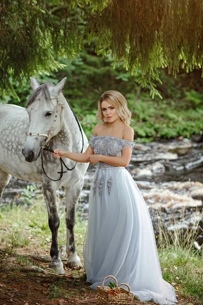 Linda menina loira esbelta no vestido abraçando um cavalo cinza, outd — Fotografia de Stock