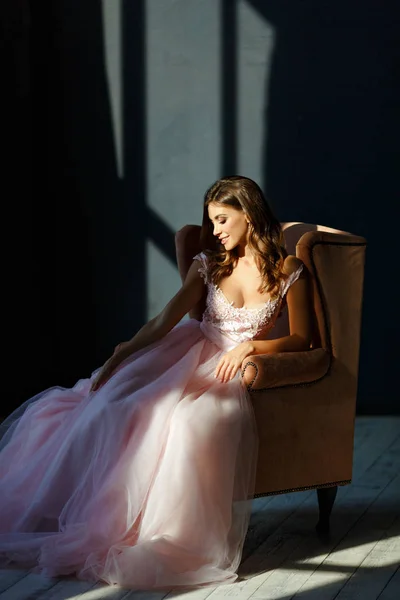 Delicada hermosa chica en un vestido rosa sonríe y se sienta en un cha —  Fotos de Stock