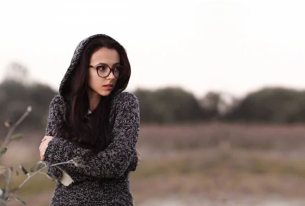 Solitario solo bella ragazza in maglione caldo con cappuccio guardando da parte in autunno campo sfondo. Immagine di una ragazza triste infelice piuttosto depressa con gli occhiali. Ragazza sola che ha una tossicodipendenza . — Foto Stock