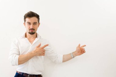 Beyaz arka planı sunarken ayakta ciddi yakışıklı adam. Parmak ile işaret ışınlama gülümseme ile genç yakışıklı işadamı.