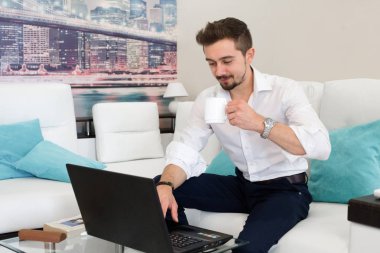 Mutlu genç adam, gözlük takıyor ve gülümsüyor. Sabahın erken saatlerinde bütün işlerini halletmek için dizüstü bilgisayarıyla çalışıyor..