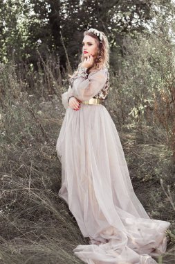 Başında bahar yeşil bahçesinde çiçek çelenk ile döngü ile uzun altın elbiseli genç güzel kız.