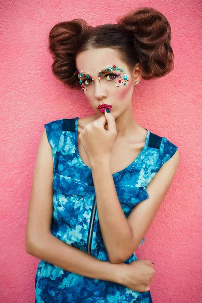 Imagen de moda del modelo de moda con dos bollos para el cabello y maquillaje profesional creativo posando sobre fondo rosa. Maquillaje creativo y peinado . — Foto de Stock