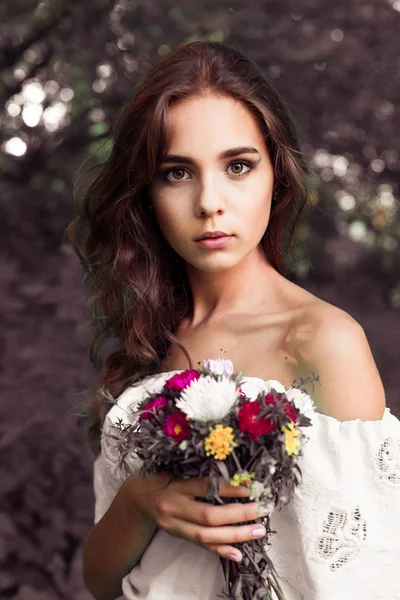 Bir buket çiçek ile güzel genç kız. Renkli çiçek duvara poz güzel mavi elbiseli güzel genç kadın. Moda fotoğraf, saçların çok güzel, gülümseyin. Gelin güzel kokulu beyaz elbiseli