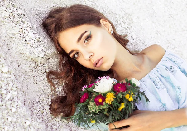 Όμορφη νεαρή γυναίκα με λεπτή λουλούδια στα χέρια της. Closeup μόδας Πορτραίτο κοριτσιού με κομψό μακιγιάζ. Όμορφο κορίτσι με μπουκέτο από λουλούδια που βλέπουν τα φωτογραφικών μηχανών. — Φωτογραφία Αρχείου