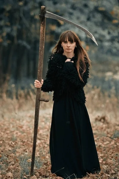 Hermosa chica misteriosa mística con el pelo largo en vestido negro sosteniendo una trenza en el bosque de otoño oscuro en el camino. Chica bonita mística en toda la ropa negra con trenza de pie en el oscuro bosque místico — Foto de Stock