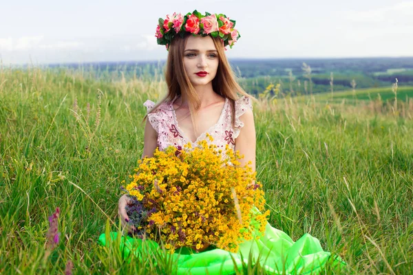 Hermosa chica bonita de moda en vestido en el campo de flores. Linda chica con corona de flores en la cabeza y ramo de muchas flores amarillas sentadas en el campo amarillo prado en verano . —  Fotos de Stock
