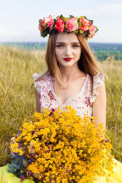 Linda menina bonita moda lindo no vestido no campo de flores. Menina agradável com grinalda de flores em sua cabeça e buquê de muitas flores amarelas sentadas no campo amarelo prado no verão . — Fotografia de Stock