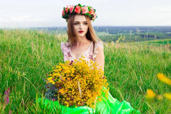 Linda menina bonita moda lindo no vestido no campo de flores. Menina agradável com grinalda de flores em sua cabeça e buquê de muitas flores amarelas sentadas no campo amarelo prado no verão . — Fotografia de Stock