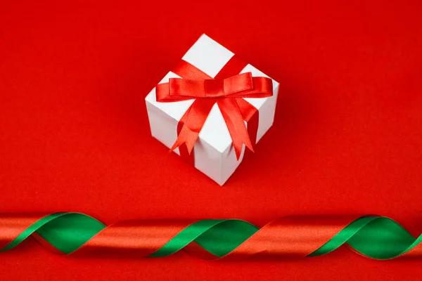Kırmızı kurdele fiyonklu kırmızı zemin üzerine beyaz hediye kutusu