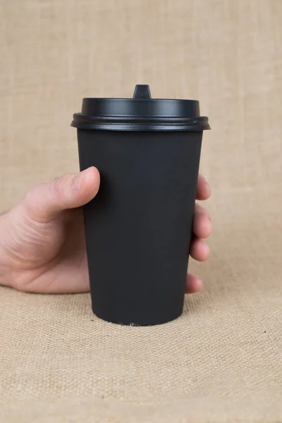 Coffee to go cup on burlap background in man hands