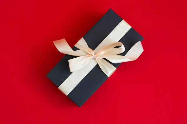 Caja de regalo negro con cinta de oro y un lazo sobre fondo rojo — Foto de Stock