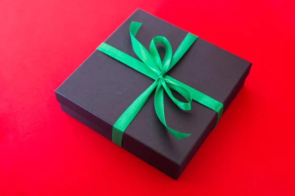 Confezione regalo nera con nastro verde e fiocco su sfondo rosso — Foto Stock