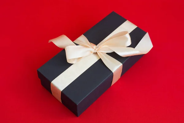 Чорна подарункова коробка з золотою стрічкою та бантом на червоному тлі — стокове фото