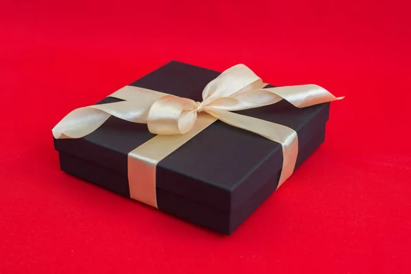 Чорна подарункова коробка з золотою стрічкою та бантом на червоному тлі — стокове фото
