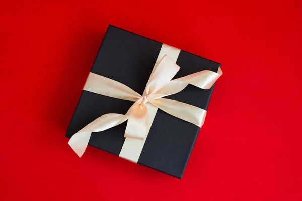 Caja de regalo negro con cinta de oro y un lazo sobre fondo rojo — Foto de Stock