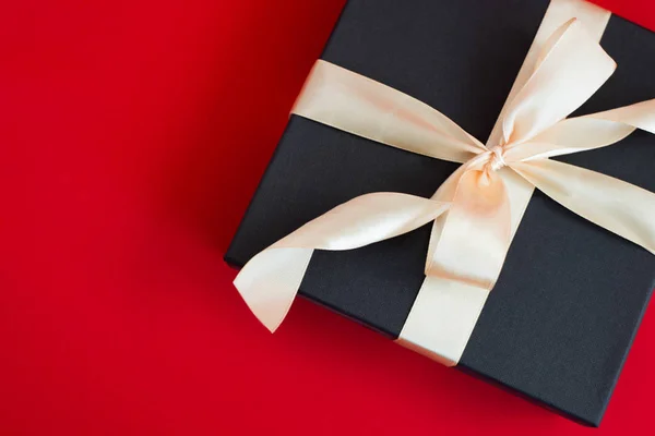 Confezione regalo nera con nastro in oro e fiocco su sfondo rosso — Foto Stock