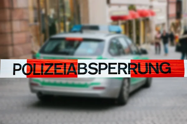 Polizeiband am Tatort. Fokus auf dem Polizeiband, ein Polizeiauto auf verschwommenem Hintergrund. deutsche Polizei. — Stockfoto