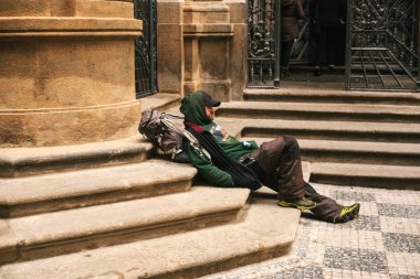 Prague, Czech Republic December 24, 2016 - Homeless hungry poor man sitting on the sidewalk in the city center. Unhappy man. Prague clipart