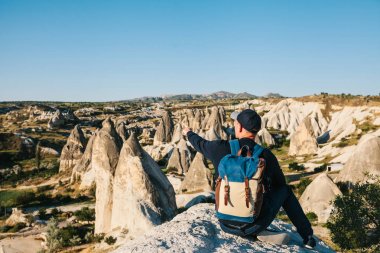 Bir gezgin bir sırt çantası ile dağlar üstüne oturur ve Kapadokya Türkiye'de güzel bir manzaraya elini gösterir. Yolculuk. Hiking.