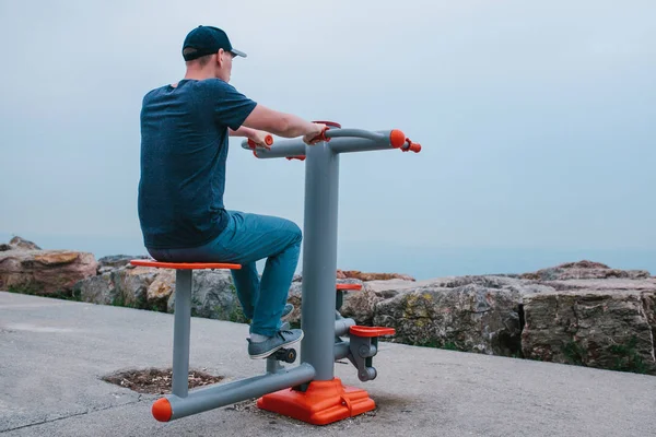 Un homme s'entraîne sur des équipements sportifs dans une ville en plein air. Le concept d'un mode de vie sain et l'accessibilité de l'entraînement sportif pour chaque personne. Équipements sportifs disponibles dans un lieu public . — Photo