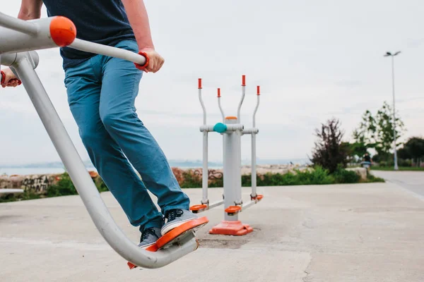 Un hombre entrena en equipo deportivo en una ciudad al aire libre. El concepto de un estilo de vida saludable y la accesibilidad del entrenamiento deportivo para cada persona. Equipamiento deportivo disponible en un lugar público . — Foto de Stock