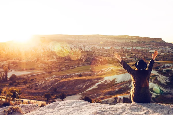Uma menina turista de chapéu senta-se em uma montanha e olha para o nascer do sol e balões na Capadócia. Turismo, turismo, Turquia . — Fotografia de Stock
