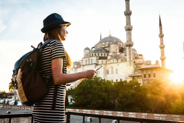 Egy fiatal gyönyörű utazó lány egy kalap egy hátizsák figyel megjelenítése mellett a Kék mecset - Isztambul híres látványa. Utazás, turizmus, városnézés. — Stock Fotó