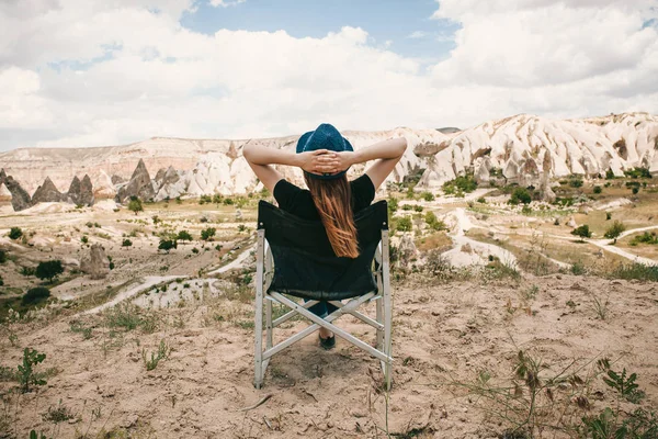 The girl sits on a chair, relaxes and admires an amazing view of the hills of Cappadocia in Turkey. Relaxation, rest, vacation, travel.