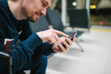 Genç bir adam ile bir bavul Havaalanı bekleme odasında oturur ve bir cep telefonu kullanır. Gece uçuşu, transfer, havaalanında bekliyor.