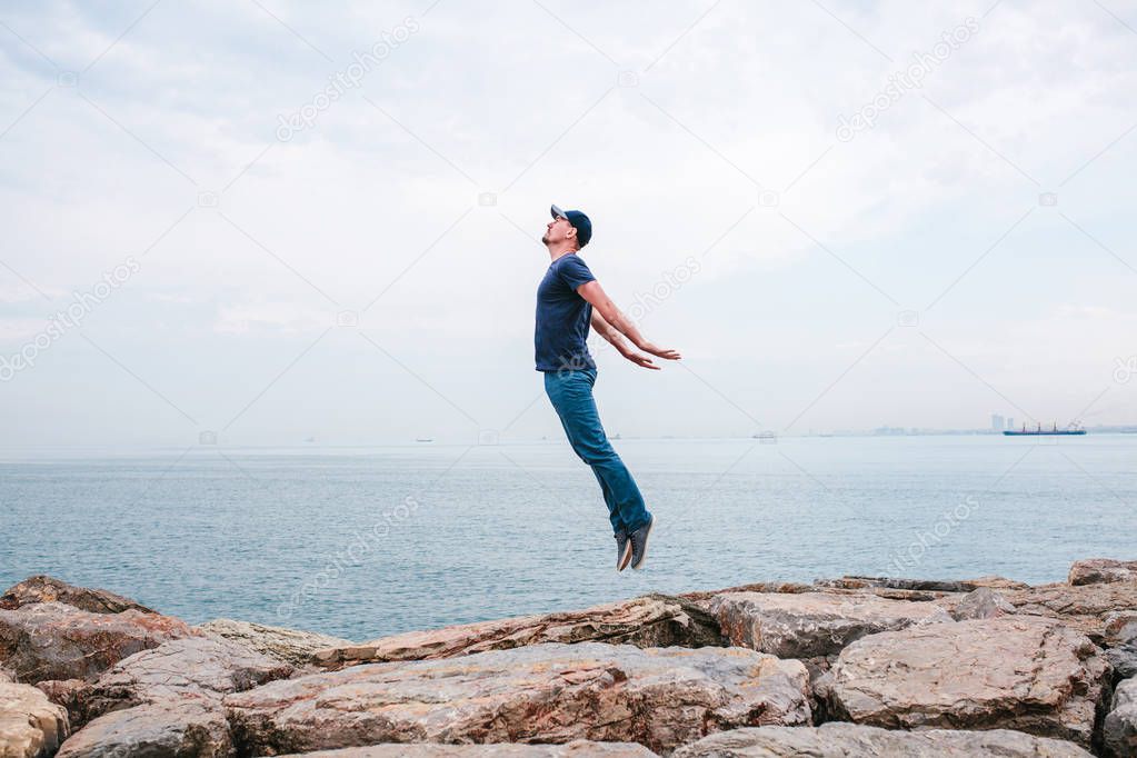 Young man jumping upwards portraying a flight against the background of the sea and sky. The concept of freedom. Life style. Travel, leisure, activity.