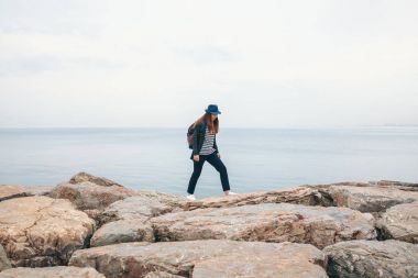 Bir gezgin bir sırt çantası ile şapkalı bir denizin yanında yürüyor. Seyahat, turizm, özgürlük.